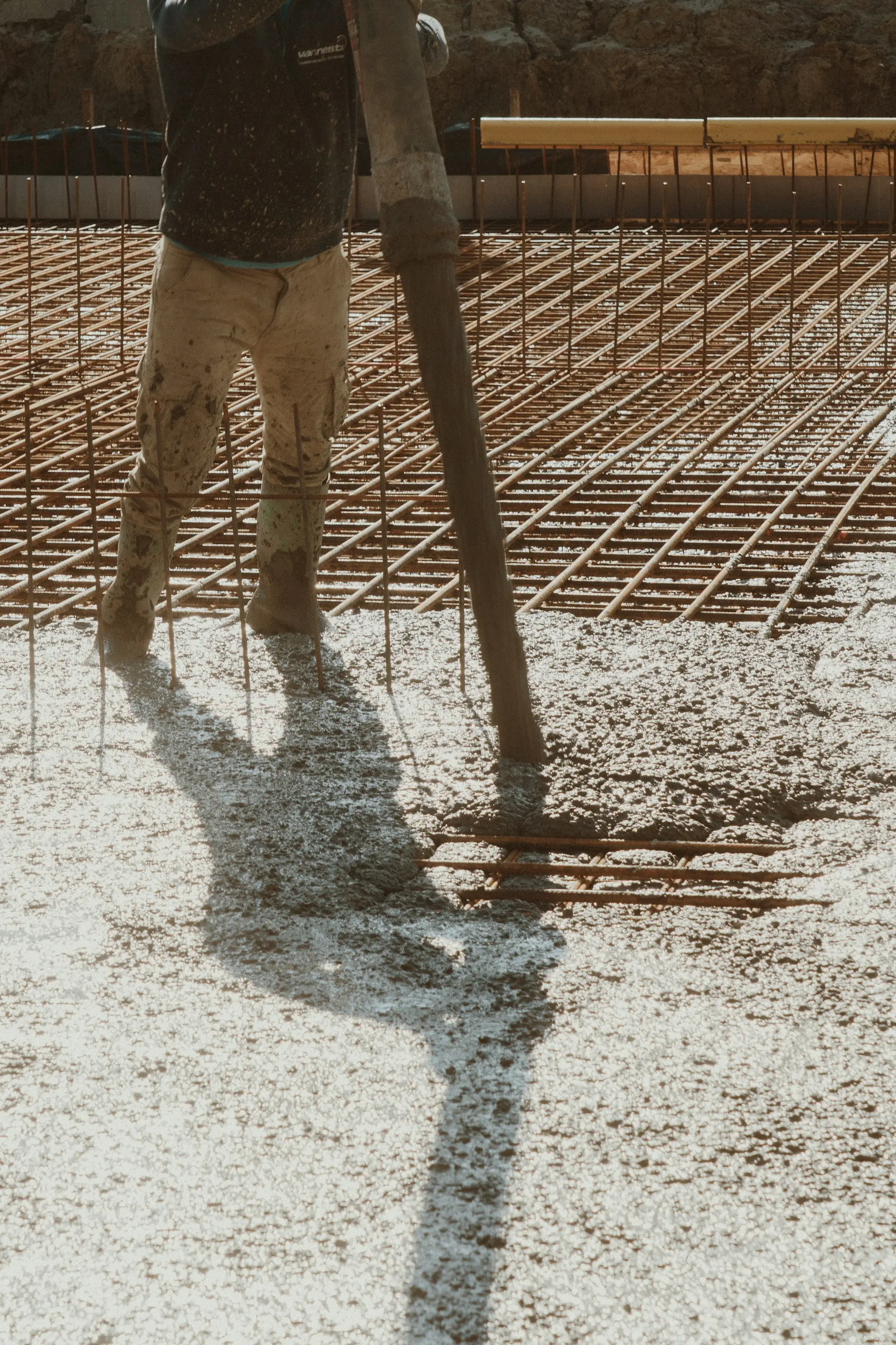 Concreter guiding a pump hose over steel reinforcing mesh while pouring a house slab