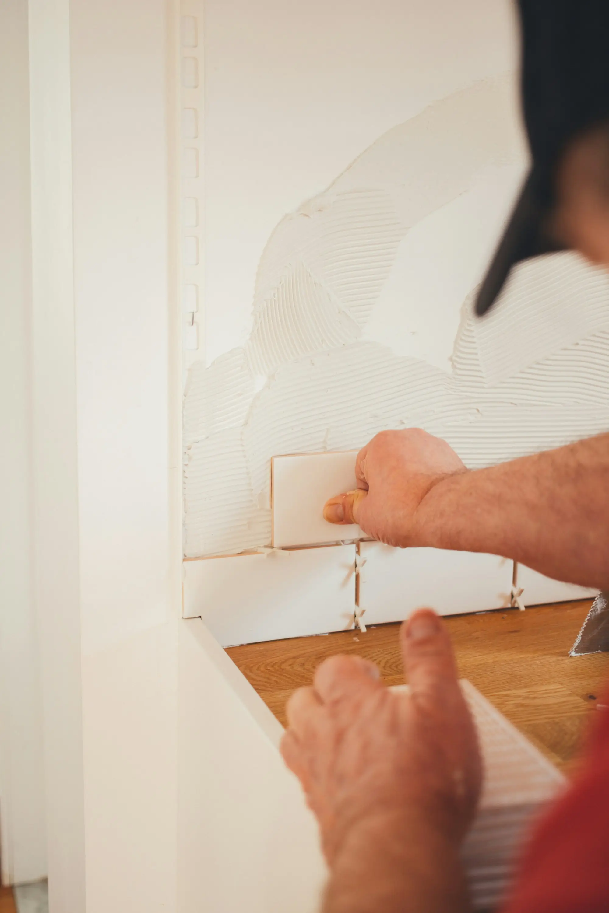 Tiler pressing a tile onto adhesive with spacers during a wall tiling job