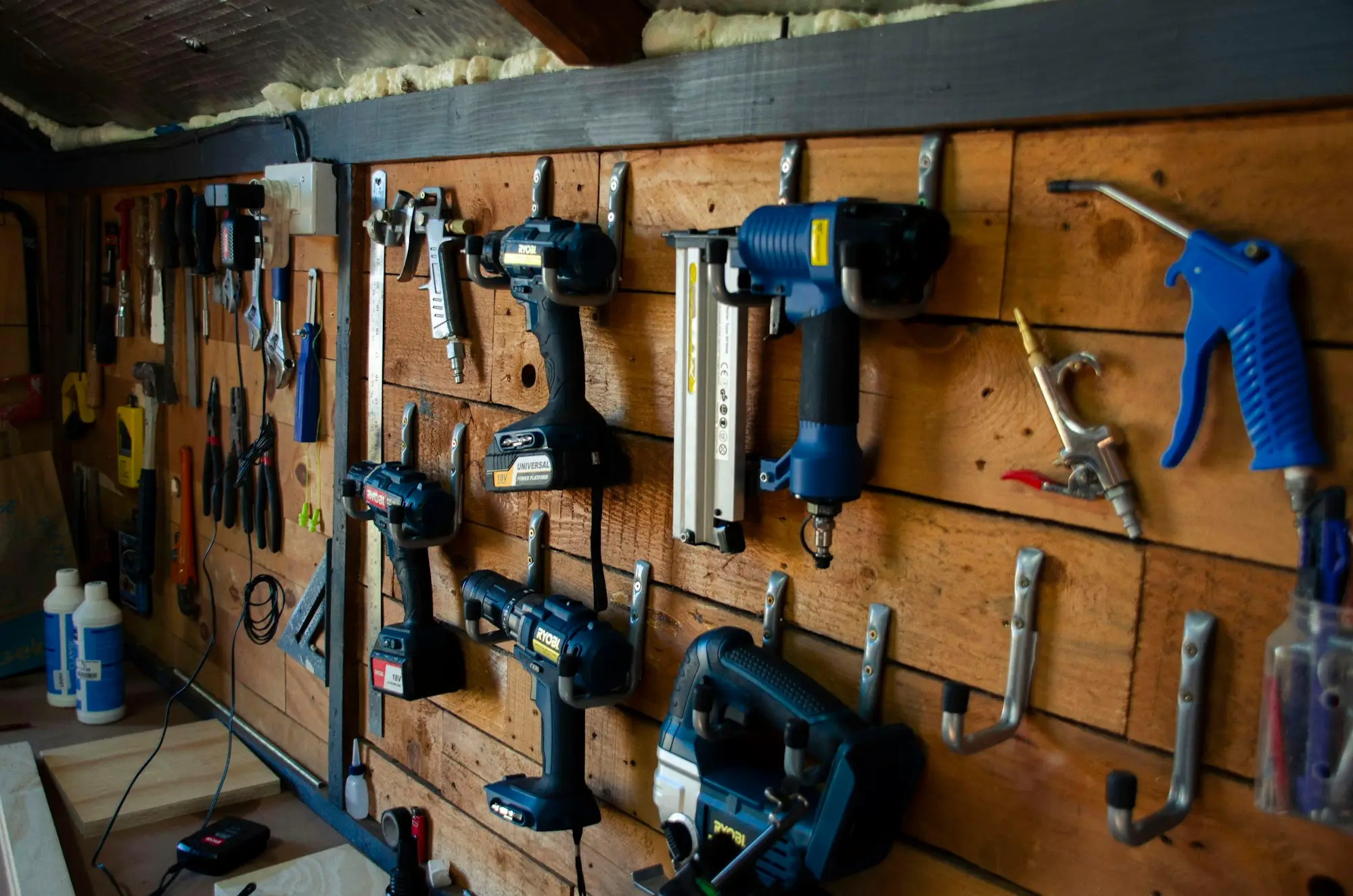 Cordless drills, a nail gun and hand tools hung on a timber workshop wall