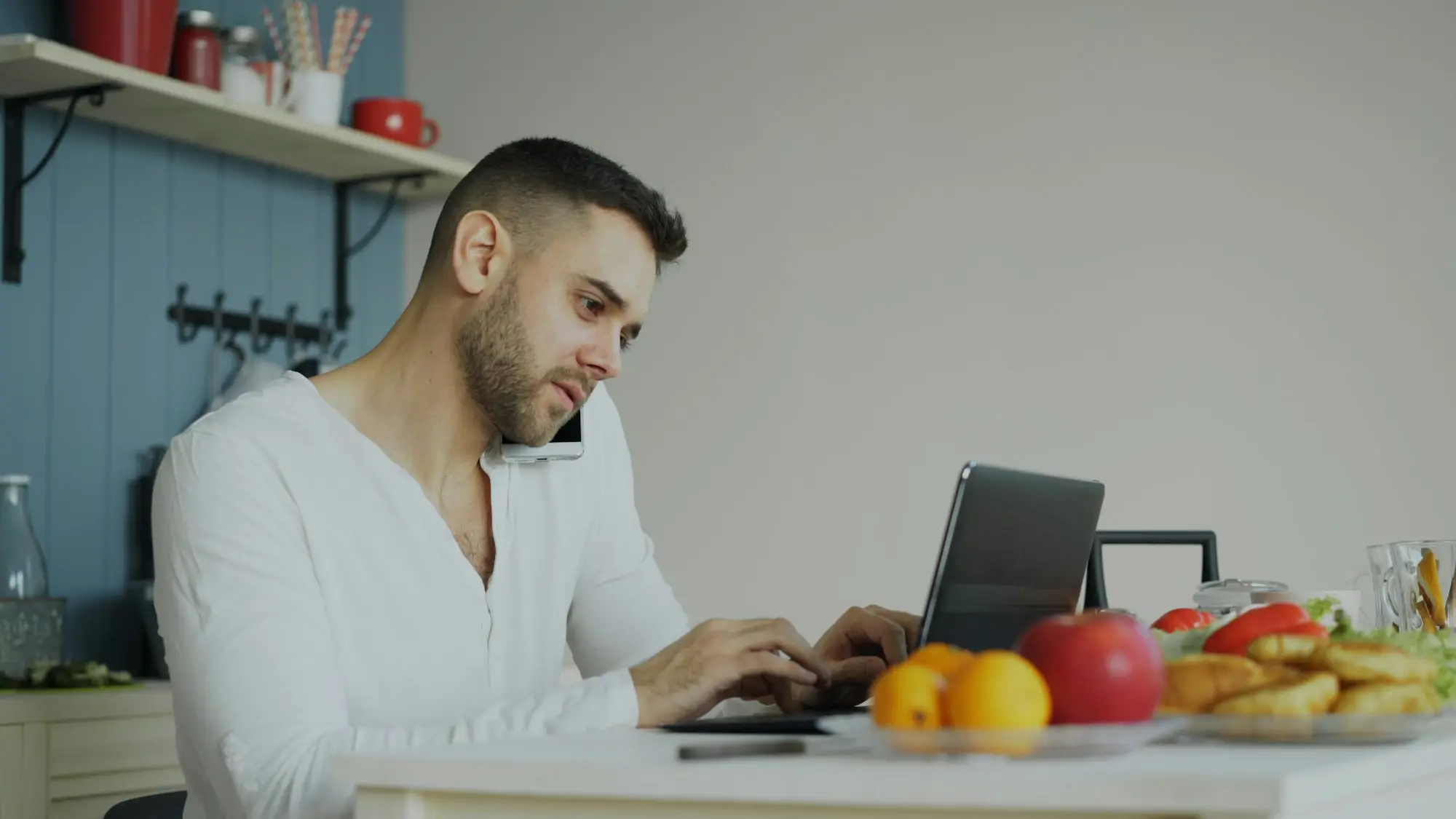 Man on the phone working at a laptop at a kitchen table